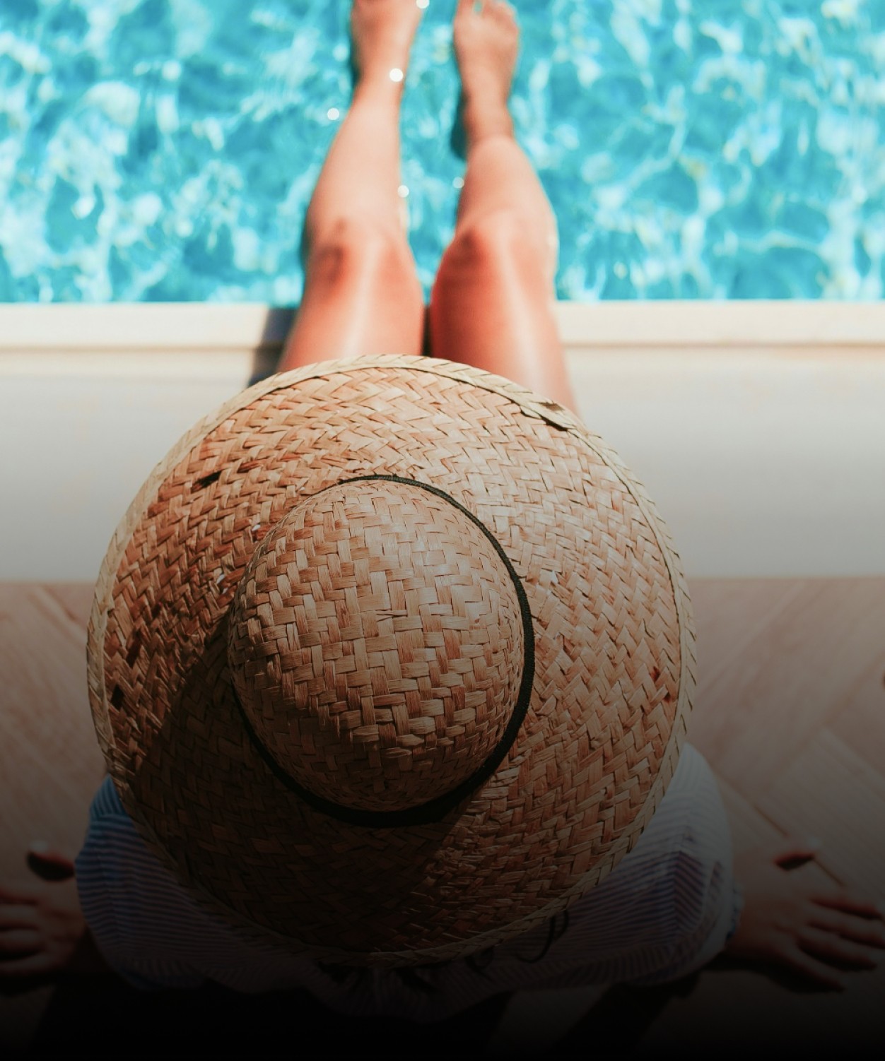 Personne se détendant au bord d'une piscine, chapeau posé sur les jambes